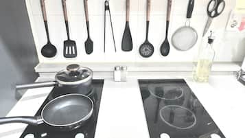 A kitchen with two induction cooktops, a range hood, and various utensils hanging on the wall.