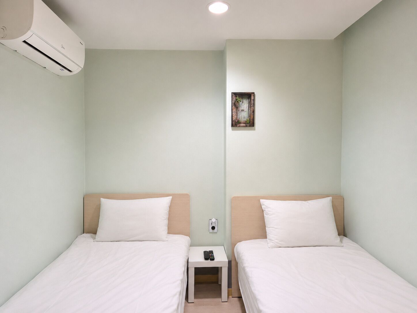 Habitación de hotel con dos camas, una mesita de noche con un control remoto y un equipo de aire acondicionado en la pared.