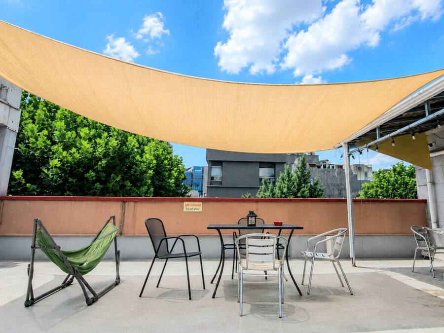 An outdoor patio with a table, chairs, a hammock, and a shade sail.