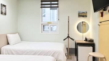 A hotel room with two beds, a small desk with a mirror, a television, and a window with blinds.