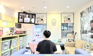 A room with a television, a clock, and a window with a view of a building. - Hostel Tommy (Seoul)