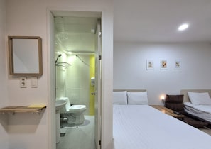 A hotel room with a bed, bedside table, and a bathroom with a toilet and sink. - Hostel Tommy (Seoul)