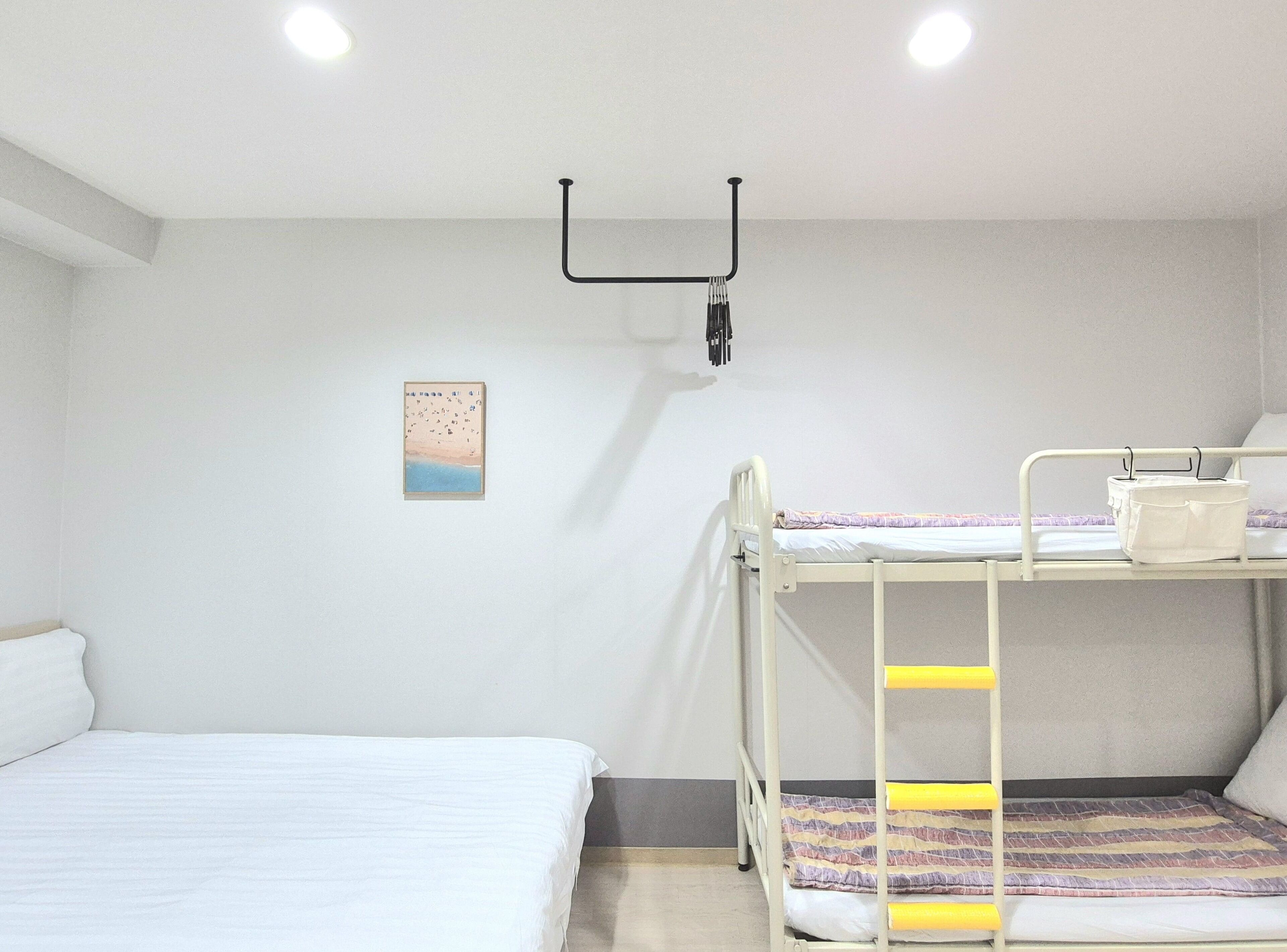 Une chambre avec un lit superposé, un lit blanc, un petit tableau encadré accroché au mur et un luminaire au plafond.