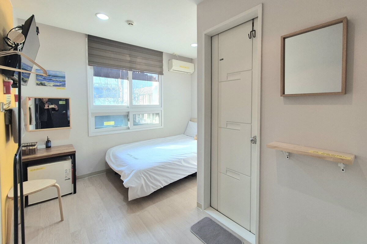A hotel room with a bed, desk, chair, and a door.