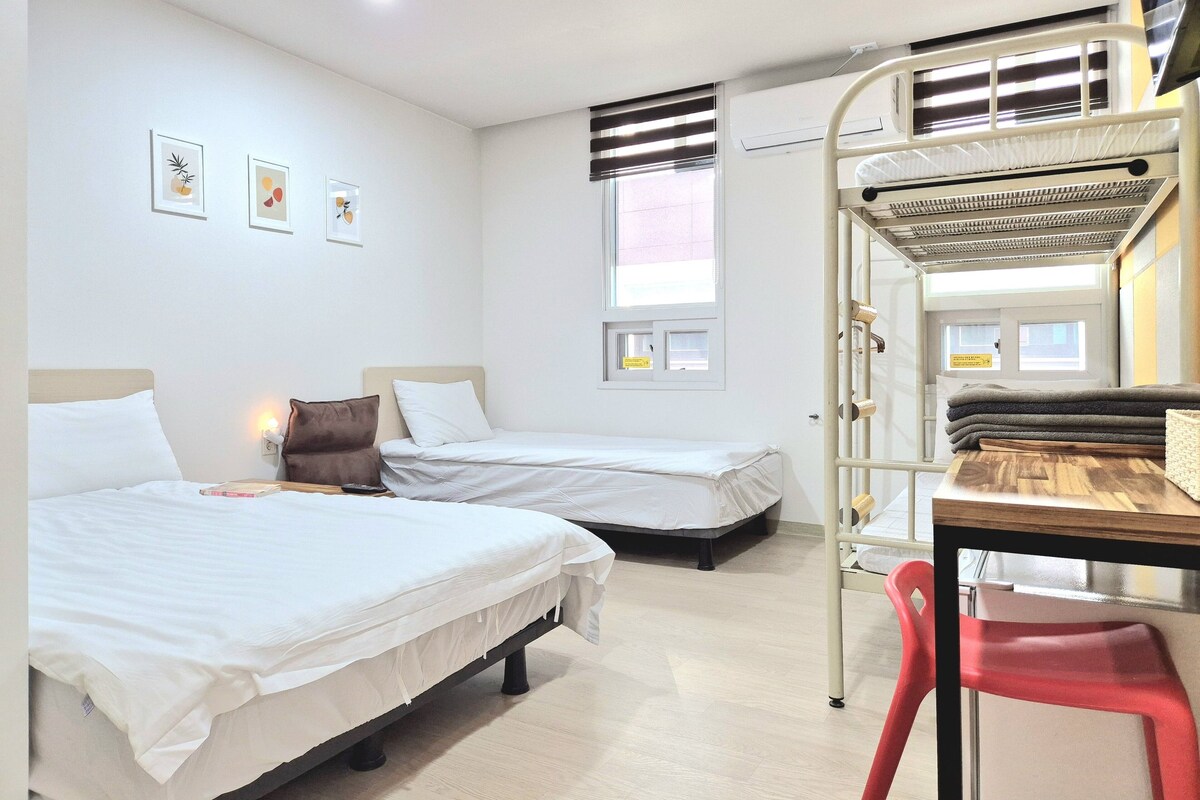 A hotel room with two single beds, a desk, and a bunk bed.