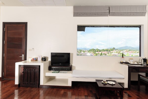 A compact hotel room with a bed, a TV, a small desk, and a window offering a scenic view.