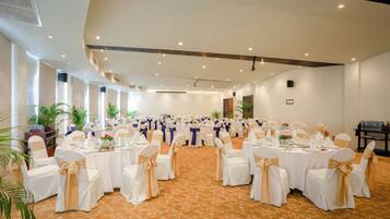 Un salón de banquetes con mesas redondas, sillas blancas con cintas doradas y una alfombra estampada.