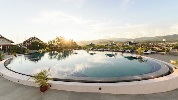 Piscina circular con sillas de descanso y sombrillas, rodeada de plantas en macetas y con vistas a montañas distantes.