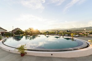 A circular pool with lounge chairs and umbrellas, surrounded by potted plants and a view of distant mountains. - Luang Prabang View Hotel (Luang Prabang)