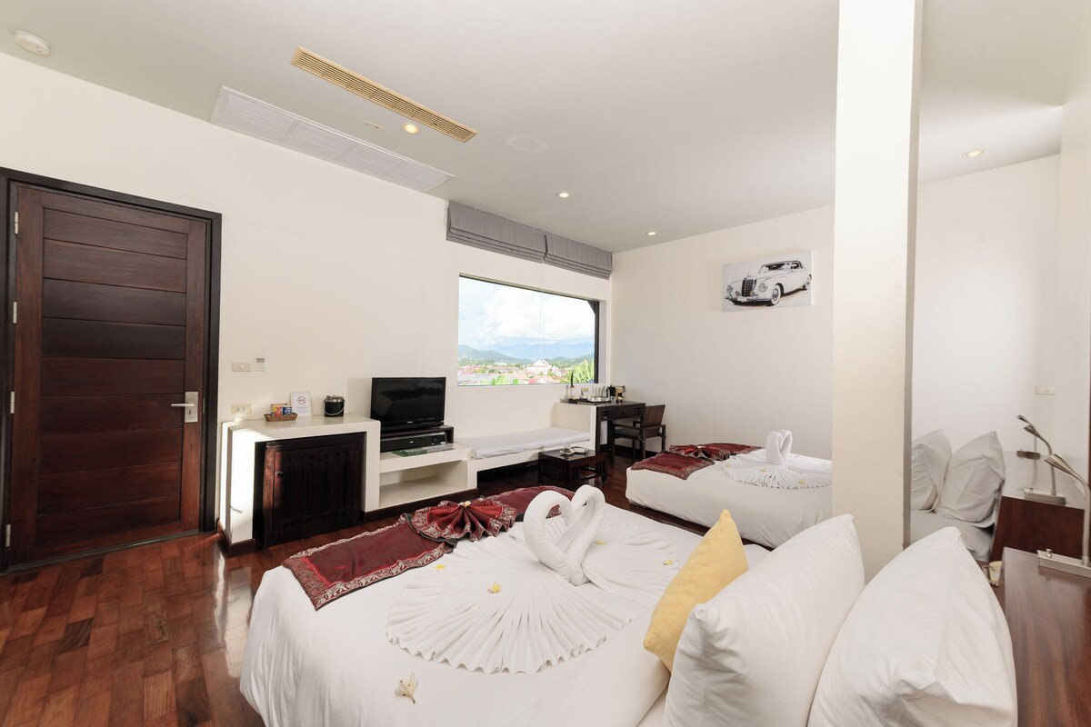 Habitación de hotel con una cama grande, un escritorio con televisor, una ventana con vistas y una puerta.