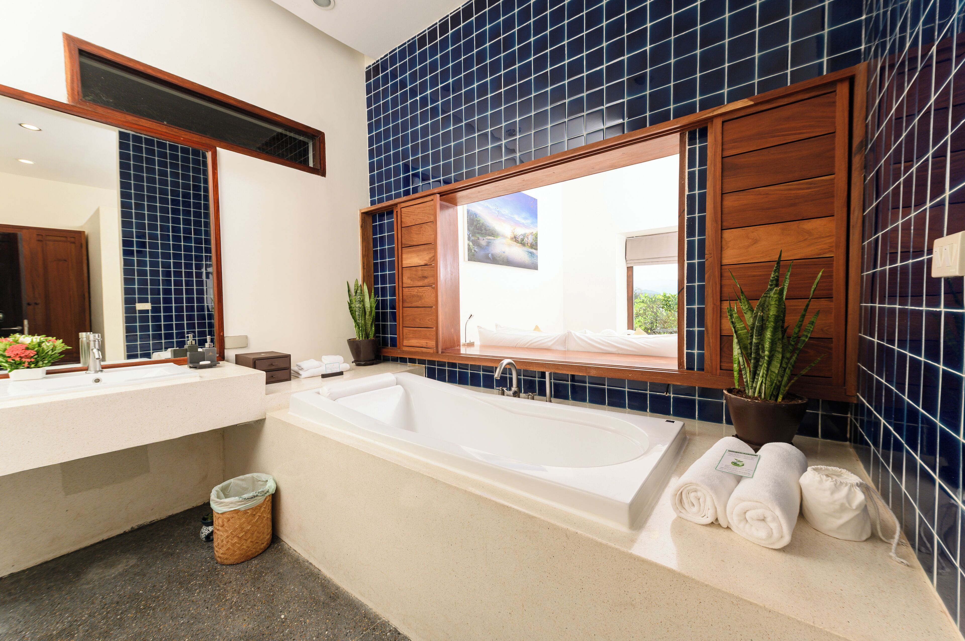 A bathroom with a large bathtub, two sinks, a window, and blue-tiled walls.