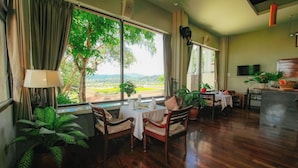 Un comedor con una mesa dispuesta para dos, ventanas amplias con cortinas y vistas a un paisaje verde.