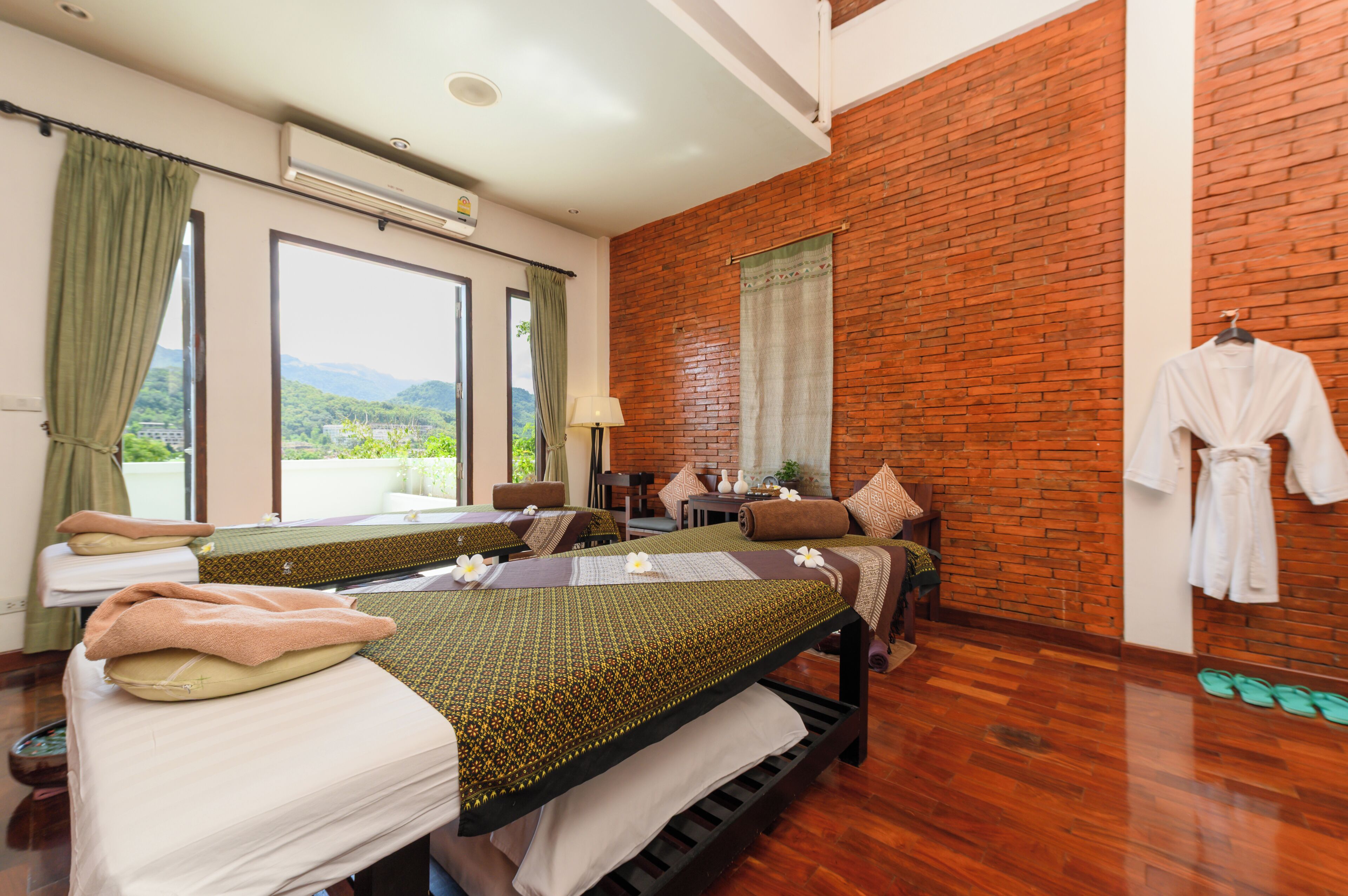 Habitación de hotel con dos camas, pared de ladrillo, vista a las montañas y una bata colgada en la pared.