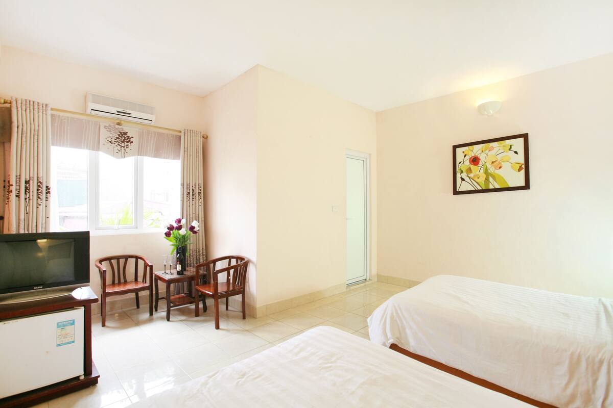 A hotel room with a bed, a TV, a desk with a chair, and a window with curtains.