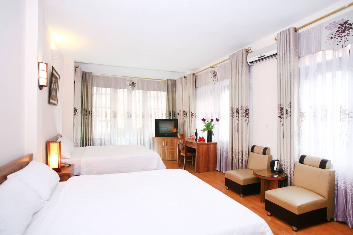 A hotel room with two beds, a desk with a chair, a TV, and a small table with a vase of flowers.