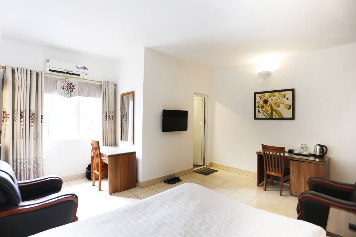 A hotel room with a bed, a desk, a chair, a television, and a painting on the wall.