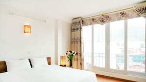 A hotel room with a large bed, a nightstand with a lamp, a vase with flowers, and a view of the outside through a large window. - Especen Hotel (Hanoi)
