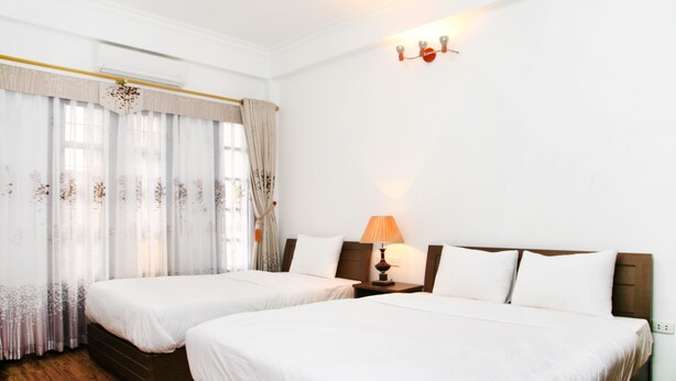 A hotel room with two single beds, a wooden floor, a nightstand with a lamp, and a window with curtains. - Especen Hotel (Hanoi)