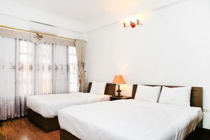 Habitación de hotel con dos camas individuales, suelo de madera, una mesita de noche con lámpara y una ventana con cortinas.