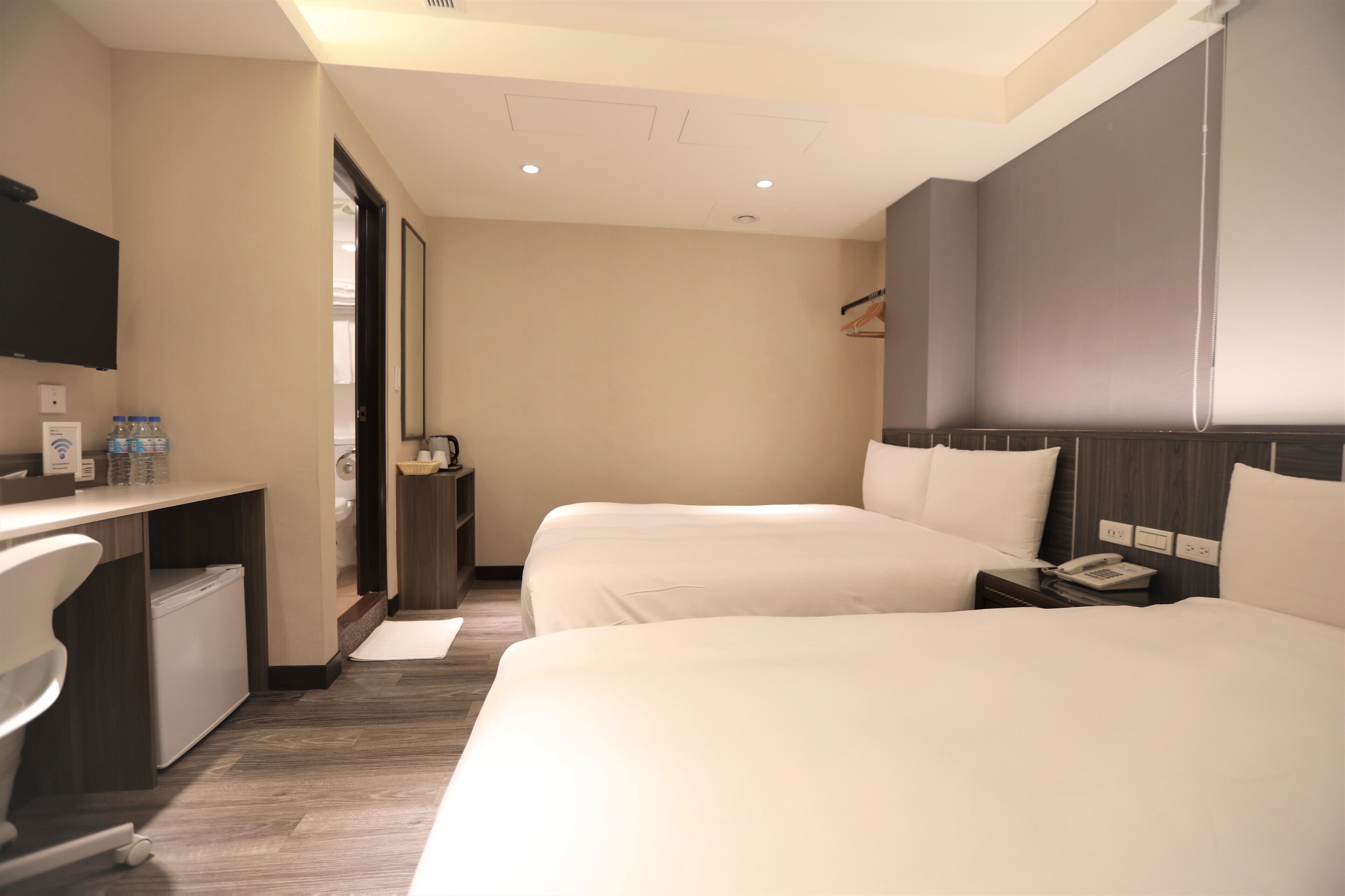 Ein Hotelzimmer mit zwei Betten, einem Schreibtisch, einem Sessel, einem Fernseher und einem Badezimmer.