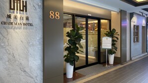Exterior do Hotel Chair Man, com fachada de mármore, o número '88' em destaque e uma entrada moderna com portas de vidro e plantas em vasos.