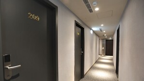 Um corredor de hotel com portas numeradas 209 e 210, um lustre moderno e um tapete estampado.