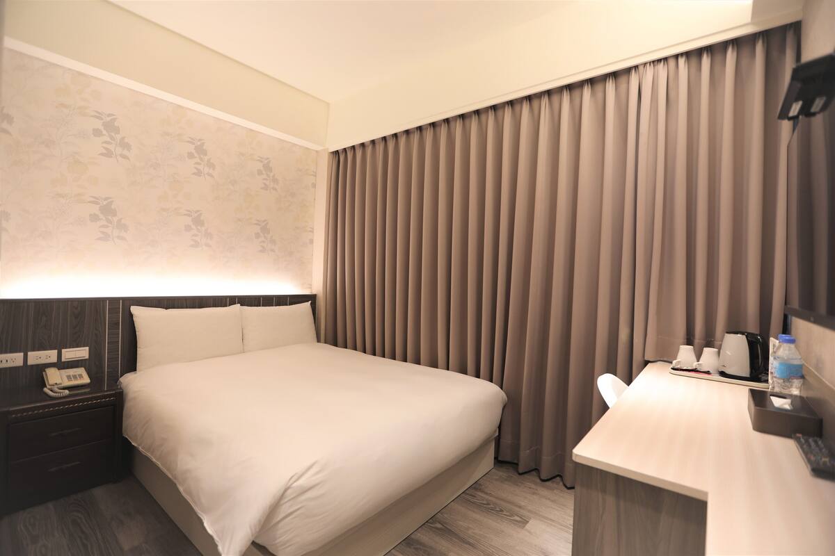 A hotel room with a large bed, a desk with a chair, a telephone, and a water bottle.