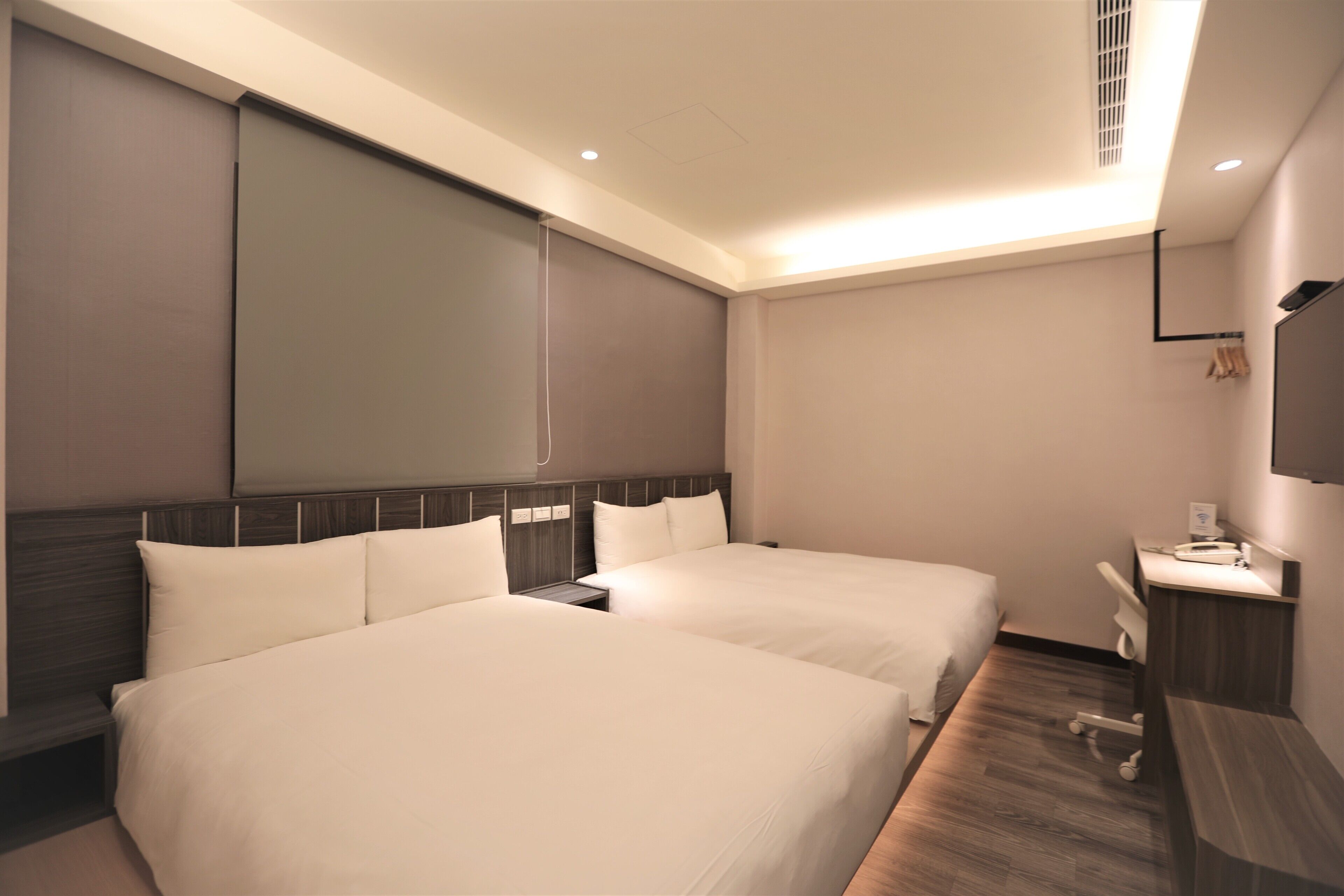 A hotel room with two beds, a desk, a chair, and a TV mounted on the wall.
