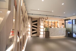 Una moderna zona de recepción con mostrador de mármol, detalles de madera y una escalera que sube a un nivel superior.