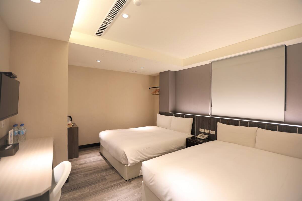 A hotel room with two beds, a desk, a chair, a TV, and a minibar.