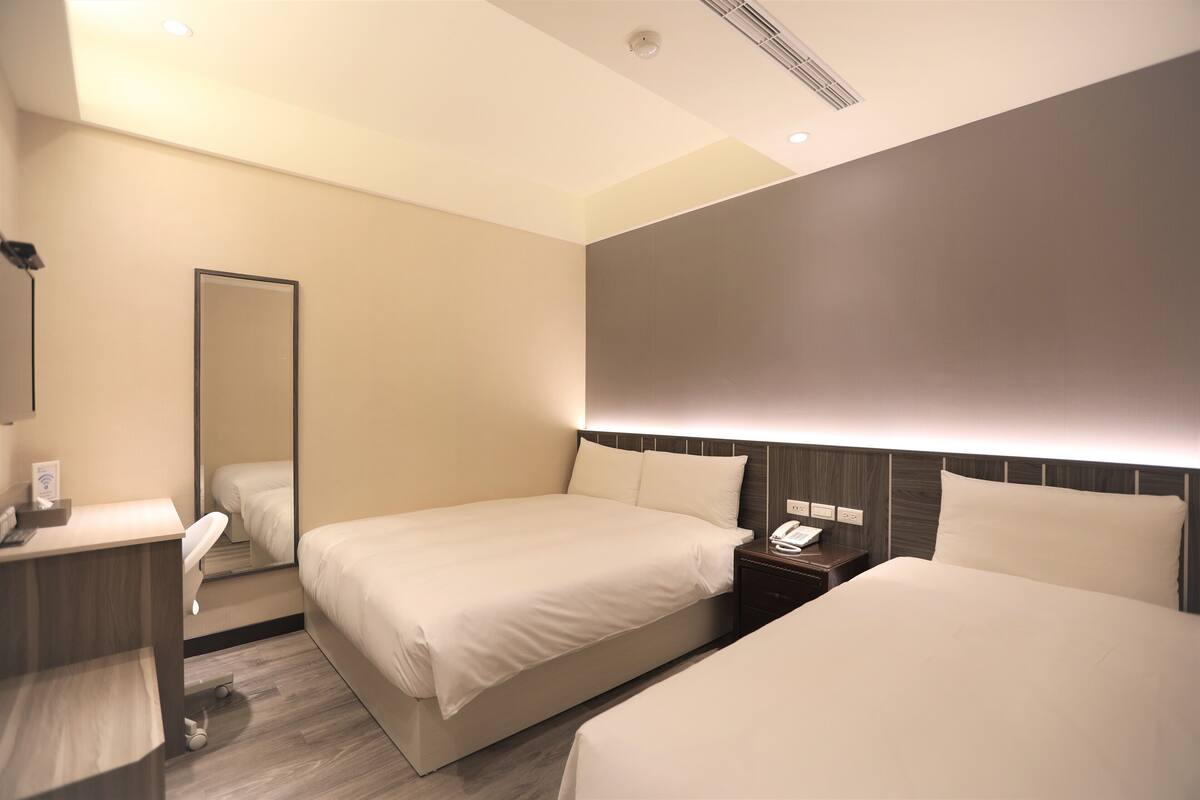 A hotel room with two beds, a bedside table with a phone, a mirror, and a wooden floor.