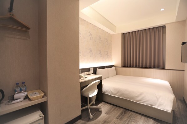Una habitación de hotel con cama, escritorio, silla y un pequeño estante con artículos de tocador.