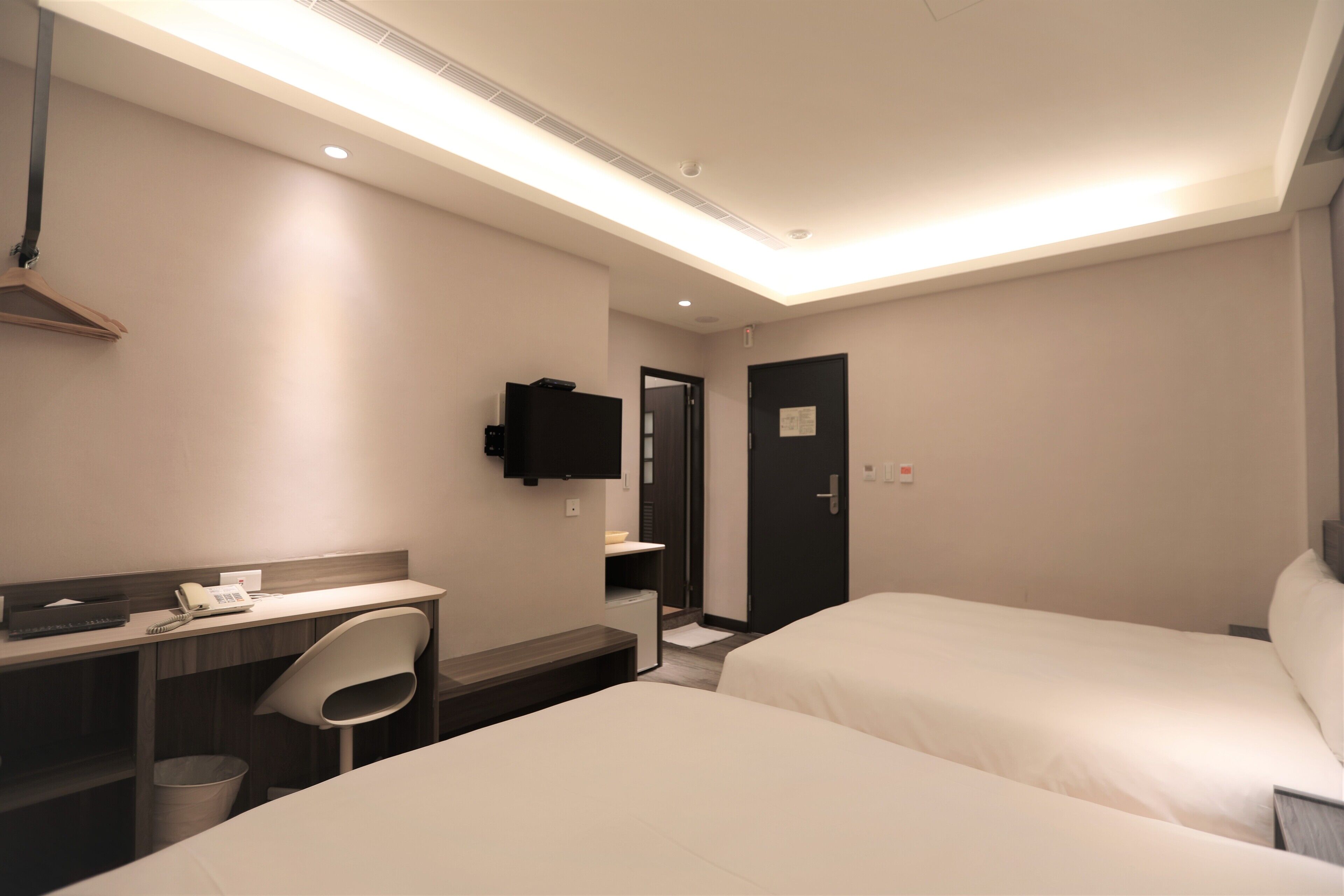 Habitació d'hotel amb escriptori, dos llits, una cadira, un safataire, un mirall i una porta.