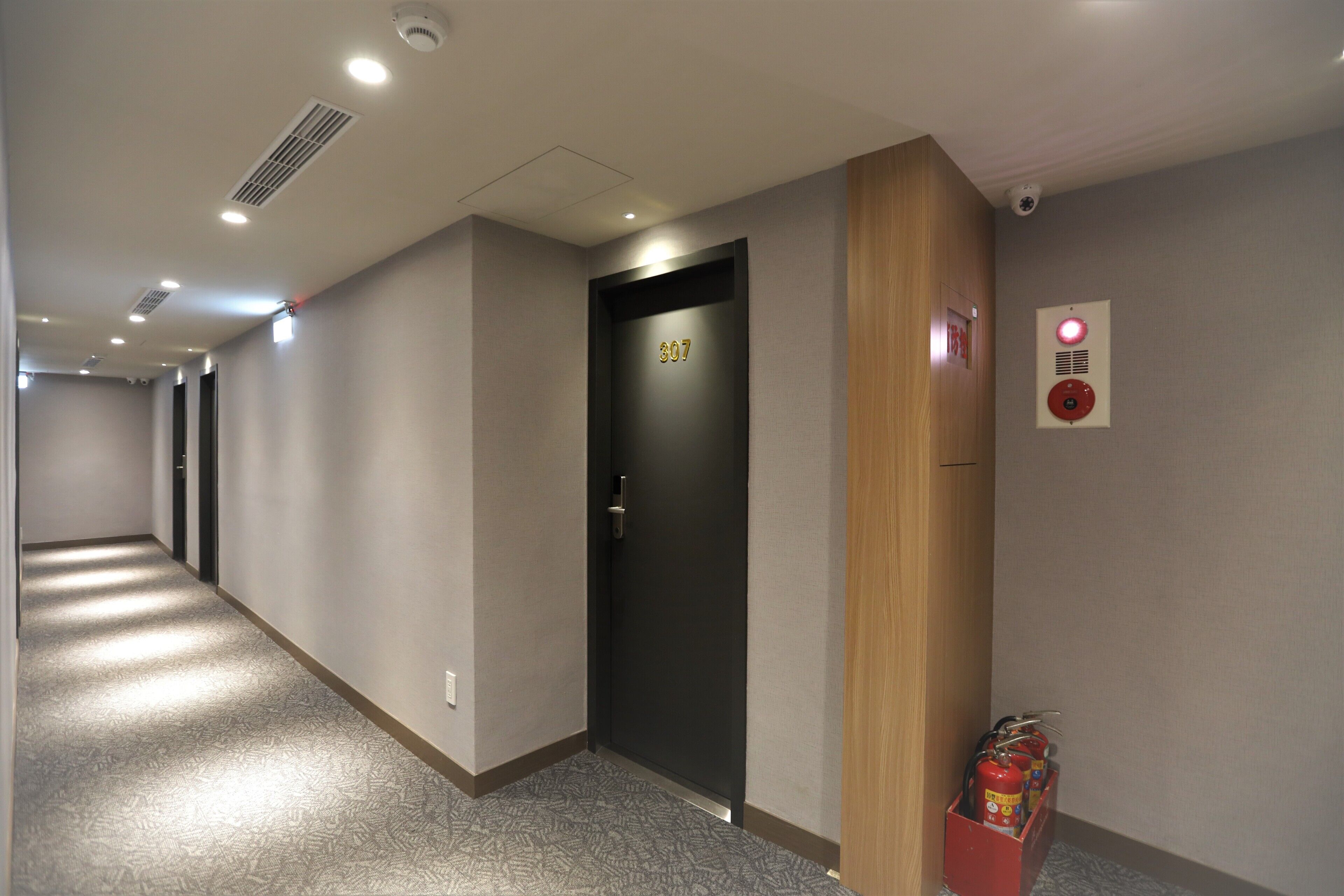 Um corredor com uma porta identificada com o número 307, um alarme de incêndio e um extintor.