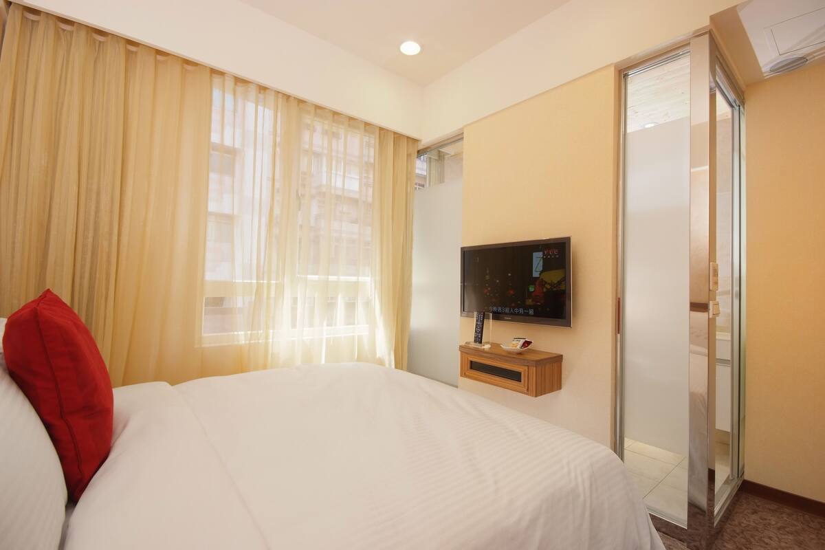 A hotel room with a bed, a TV on the wall, and a sliding door to the bathroom.