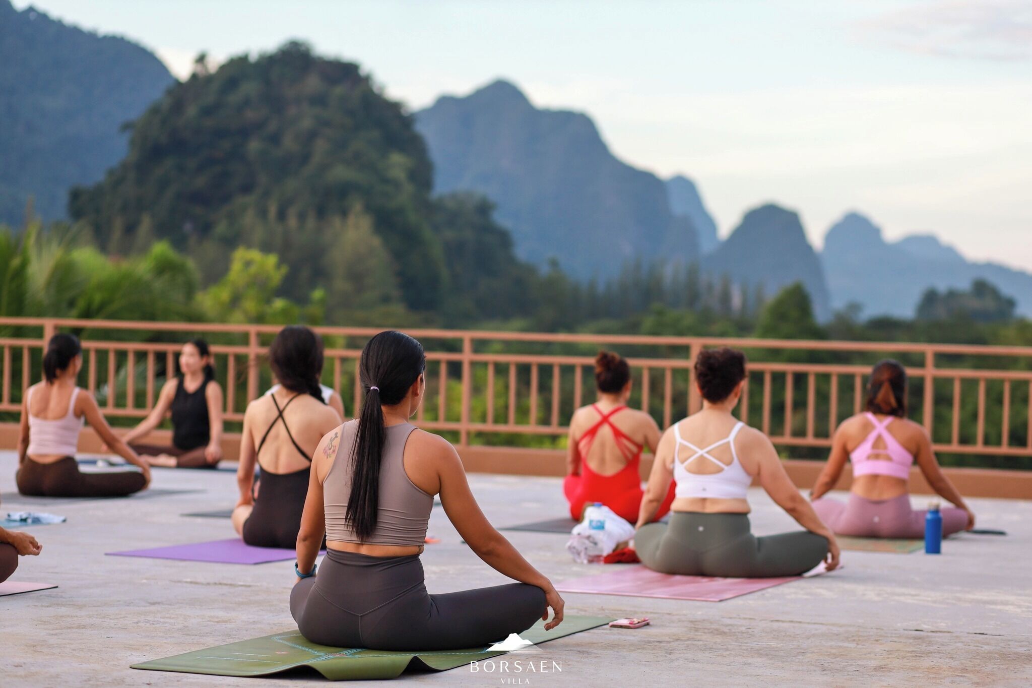 A group of people sitting on yoga mats outdoors with a mountainous backdrop.