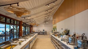 Un moderno bufé de desayuno con múltiples estaciones de servicio, un techo alto con luminarias únicas y grandes ventanales que ofrecen vistas al exterior.