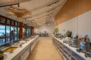 Un moderno bufé de desayuno con múltiples estaciones de servicio, un techo alto con luminarias  únicas y grandes ventanales que ofrecen vistas al exterior.