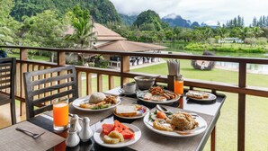 Una mesa de comedor con platos de comida, un vaso de jugo de naranja y vistas a un lago y montañas.
