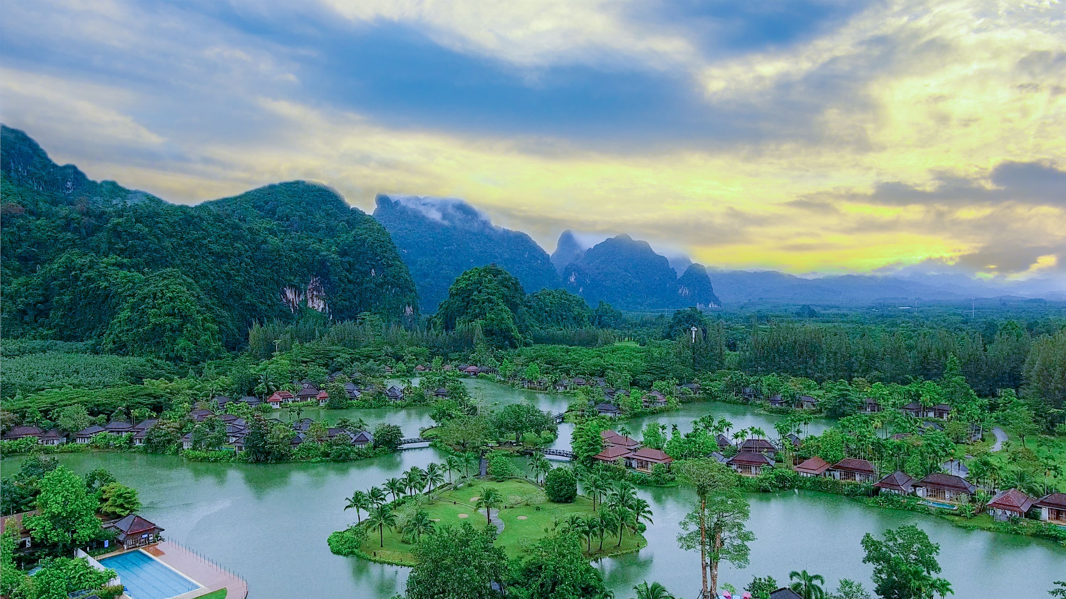 Een resort met meerdere bungalows, omgeven door weelderige begroeiing en een meer.