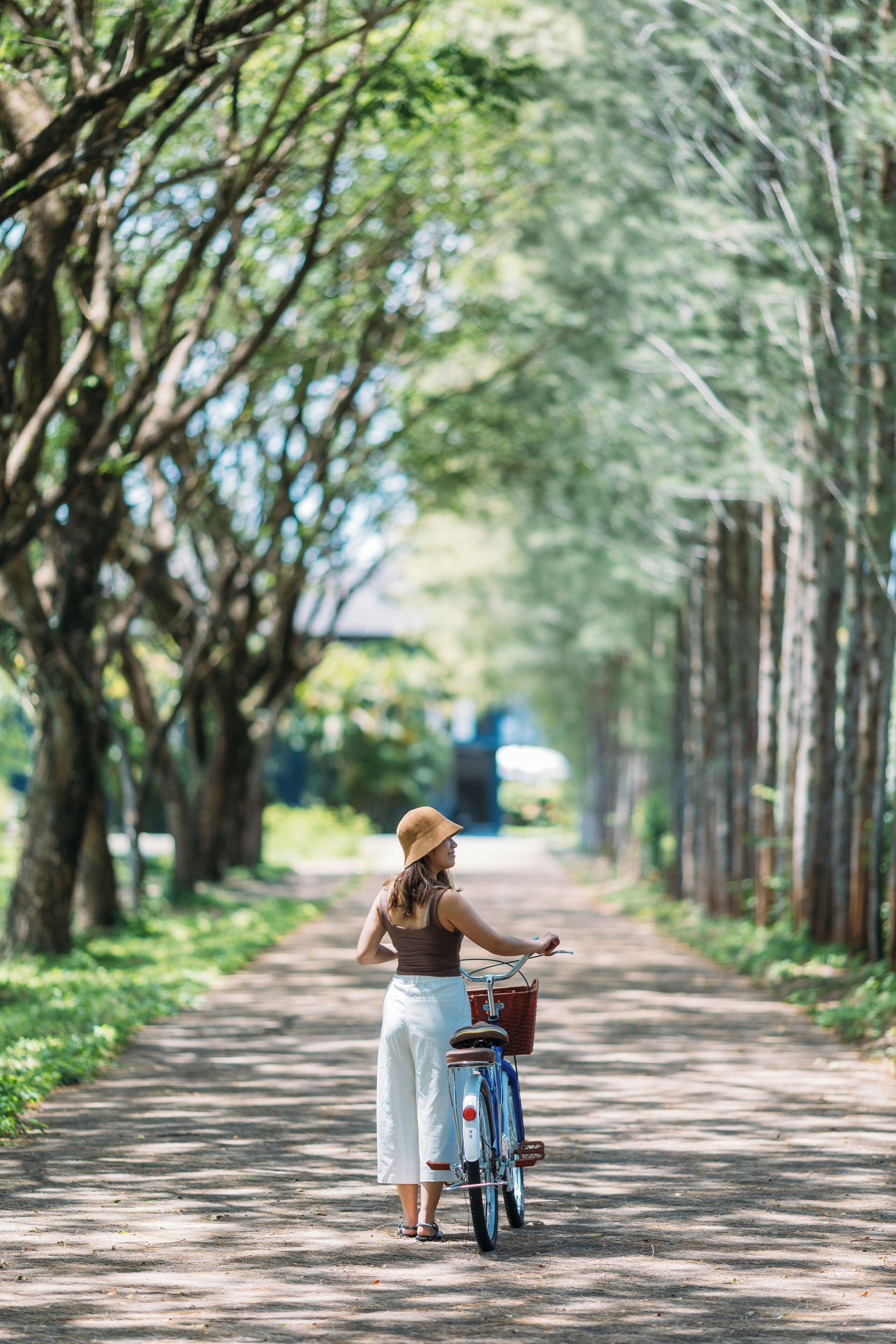 A woman standing beside a bicycle on a tree-lined path.