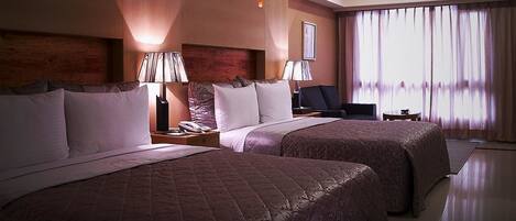 A hotel room with two beds, a desk, a chair, and a large window with curtains.