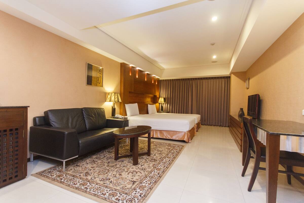 A hotel room with a bed, a sofa, a coffee table, a TV, and a desk.