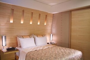 A hotel room with a wooden headboard, a bed with a quilted cover, two bedside tables with lamps, and a telephone.