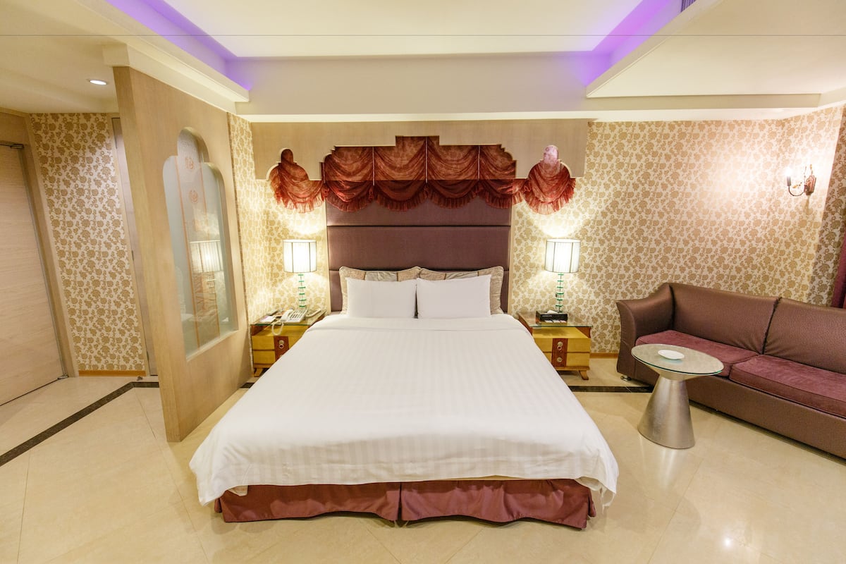 A hotel room with a large bed, two bedside tables with lamps, a sofa, and a small round table.