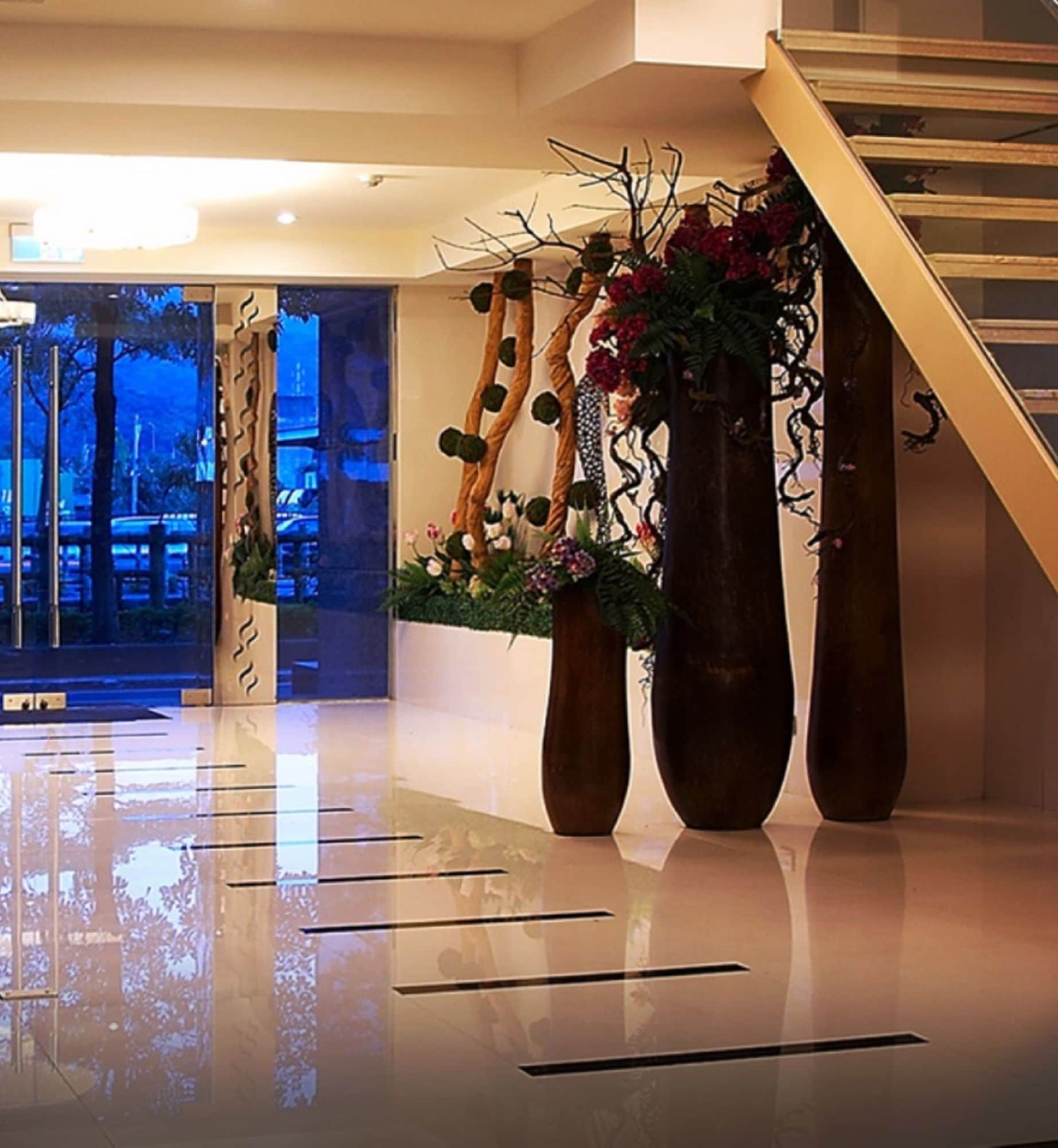A modern lobby with a reflective floor, a staircase, and decorative vases with flowers.