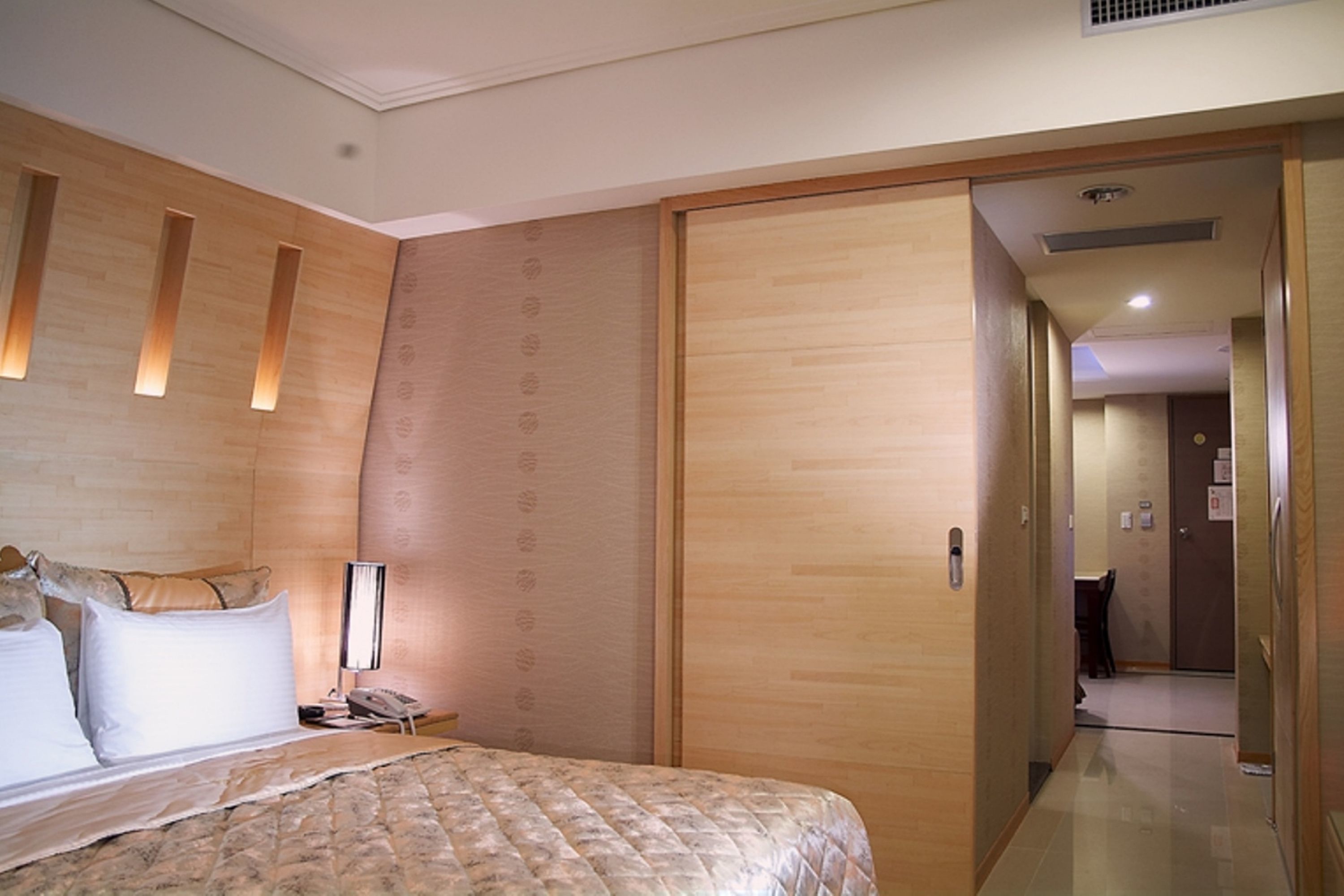 A hotel room with a bed, a bedside table with a lamp, a telephone, and a wardrobe.