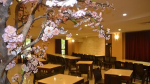 A restaurant with tables and chairs arranged in rows, a decorative tree with pink blossoms, and a red curtain in the background. - SLV Hotel Group - SLV Business Hotel (New Taipei City)
