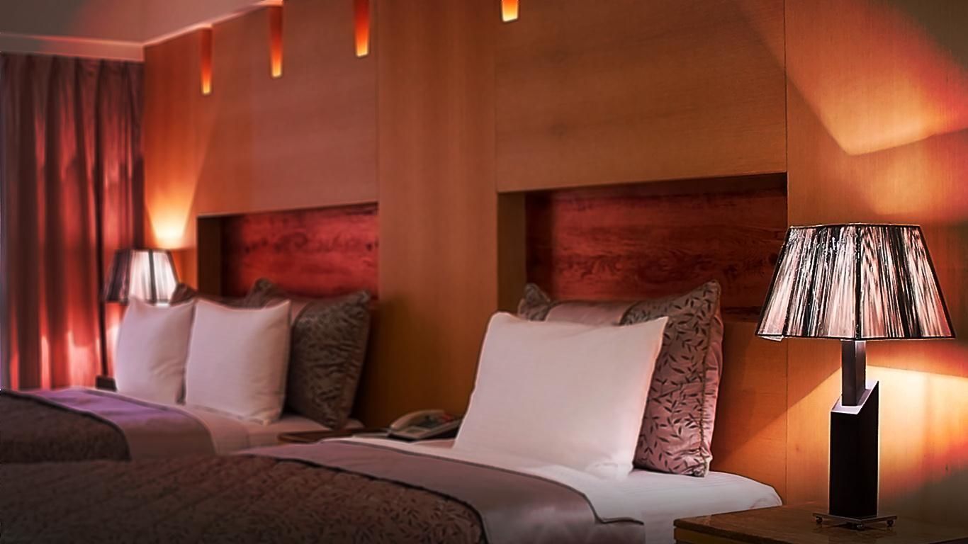 A hotel room with two beds, a nightstand with a lamp, and a large window with curtains.