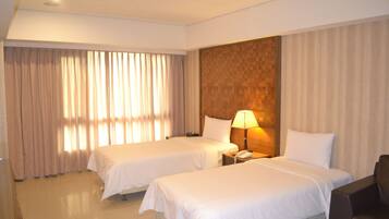 A hotel room with two beds, a nightstand with a lamp, a chair, and a large window with curtains.